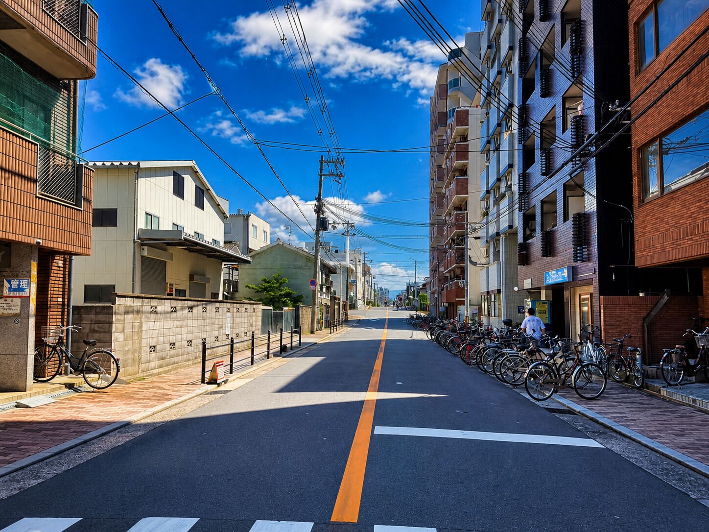 A street lined with residential buildings, a clear sky, and a bicycle parking area.