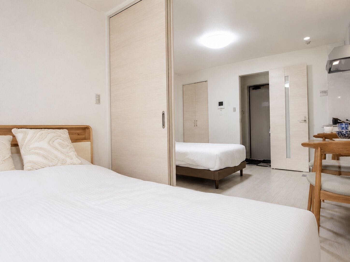 A bedroom with a bed, a wooden nightstand, a wardrobe, and a door leading to another room.