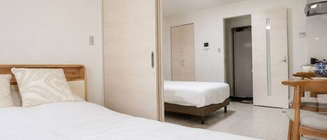 A bedroom with a bed, a wooden nightstand, a wardrobe, and a door leading to another room.