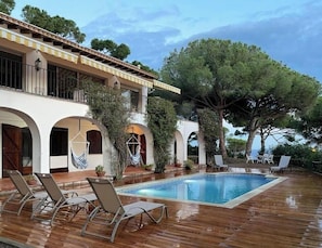 A poolside area with lounge chairs, a swimming pool, and a building with arched windows and a tiled roof. - Mediterranean villa with sea views, Lloret de Mar (Lloret de Mar)