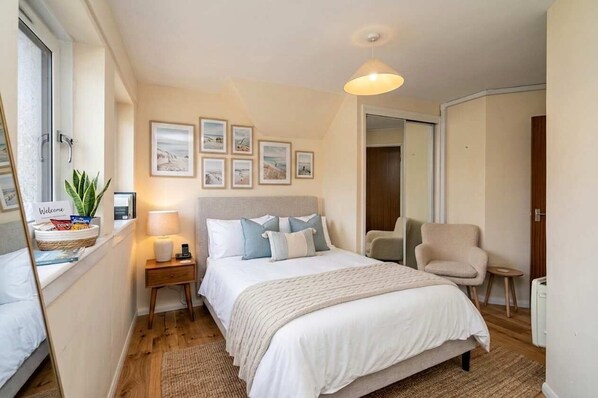 A bedroom with a bed, bedside tables, a chair, a lamp, and framed pictures on the wall.