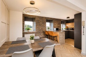 Una cocina moderna con salpicadero de piedra, un comedor con mesa y sillas de madera, y un ventanal que proporciona luz natural.
