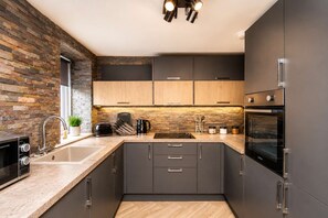A modern kitchen with a stone backsplash, dark cabinets, a built-in oven, and a stainless steel range hood. - Nr Gala Water walks & countryside trails -WiFi-5BR (Scottish Borders)