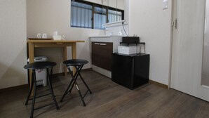 Een kleine kitchenette met een koelkast, een spoelbak en een raam. Er staan twee krukken bij een tafel met bekers en een zakdoos.