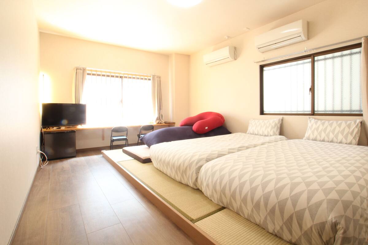 Una habitación de hotel con cama, escritorio, silla, televisor y aire acondicionado.