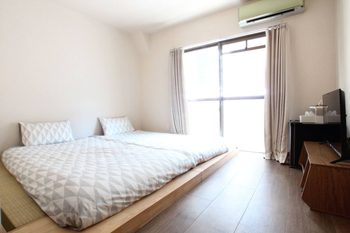 Un dormitorio con cama, escritorio, aire acondicionado y ventana con cortinas.