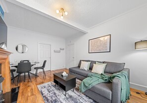 Ein modernes Wohnzimmer mit einem grauen Sofa, einem Couchtisch, einem Essbereich mit Stühlen und einem Kamin.