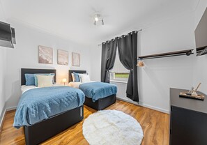 A bedroom with two beds, a white fluffy rug, a desk, and a window with curtains. - Traditional 2 bedroom ground floor apartment (Hamilton)