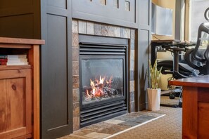 Une cheminée avec un feu de bois, un meuble en bois et un bureau avec une chaise.