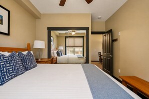 A hotel room with a large bed, a desk, a chair, a window with blinds, and a door.