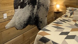 Ein Zimmer mit Holzwänden, einer großen Tierfell-Dekoration an der Wand, einem Bett mit gemusterten Bettwäsche und einem Nachttisch mit Lampe.
