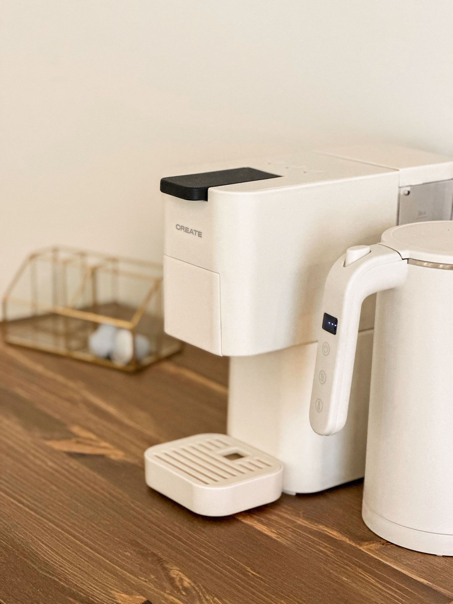 Una cafetera con panel de control y una tetera sobre una mesa de madera.