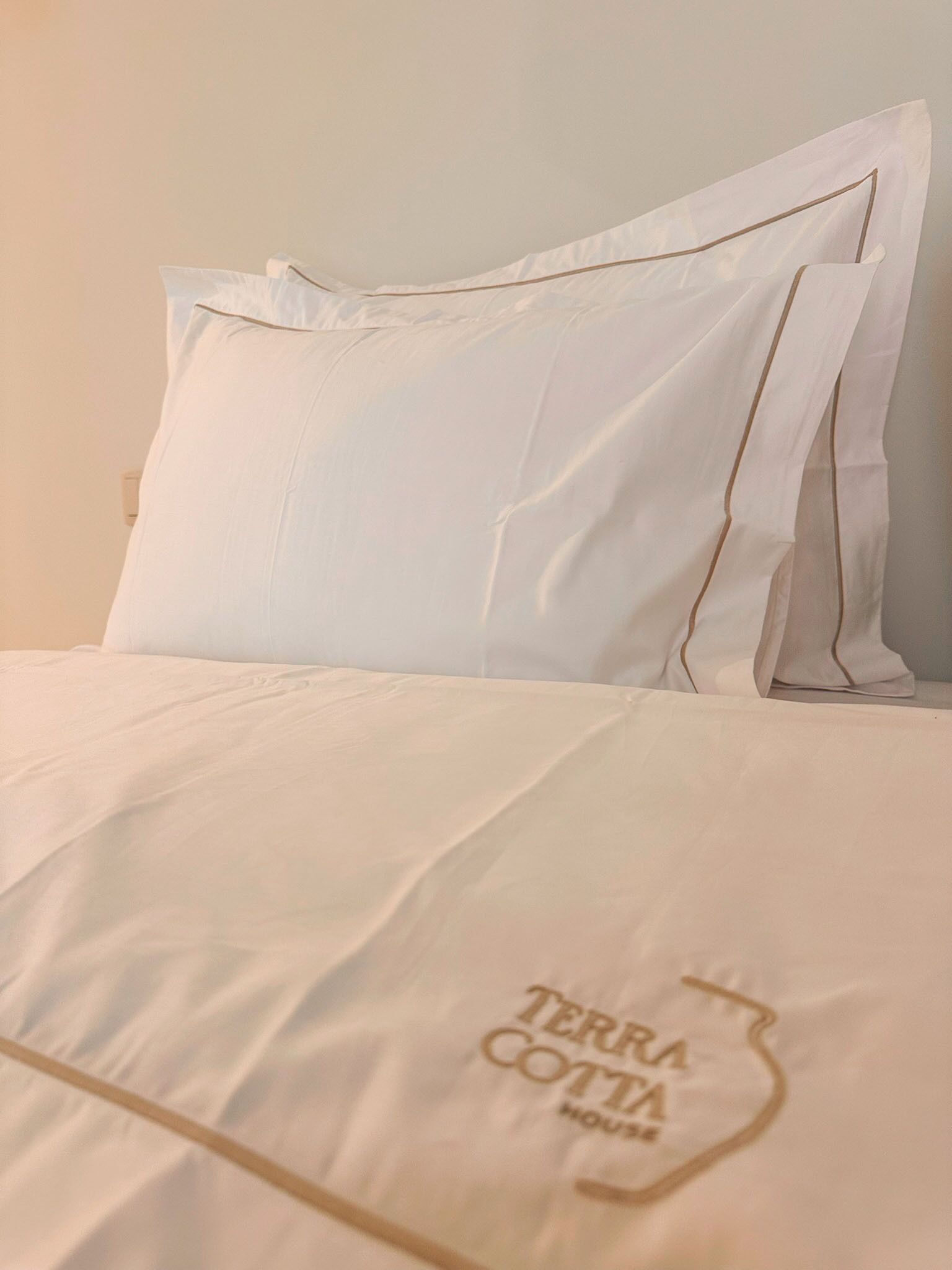Una cama con ropa blanca y una almohada con el texto 'TERRA COTTA HOUSE'.