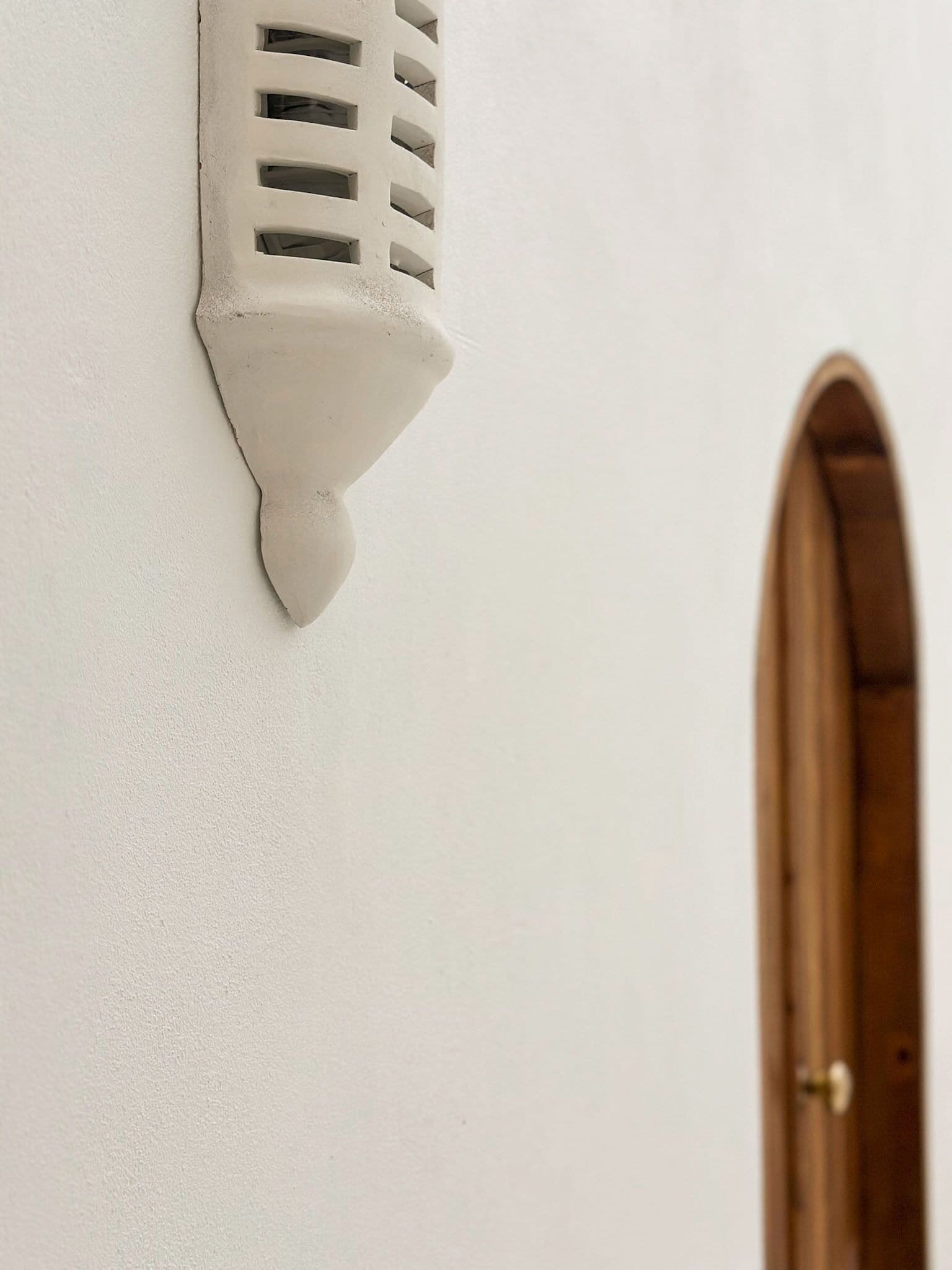 A white wall with a textured, white, decorative wall piece and a wooden door.
