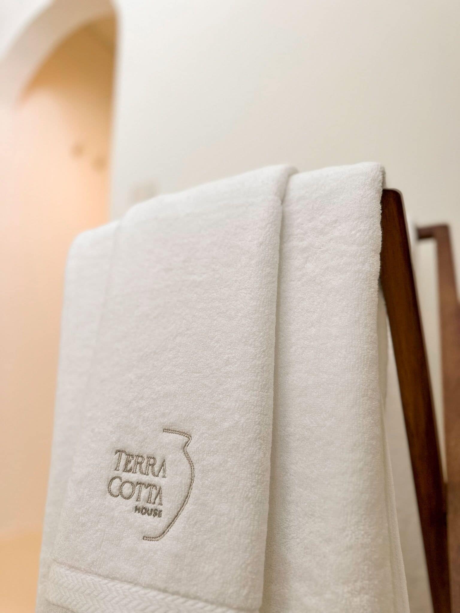 A white towel with 'TERRA COTTA HOUSE' embroidered on it, folded on a wooden chair.