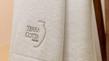 A white towel with 'TERRA COTTA HOUSE' embroidered on it, folded on a wooden chair.