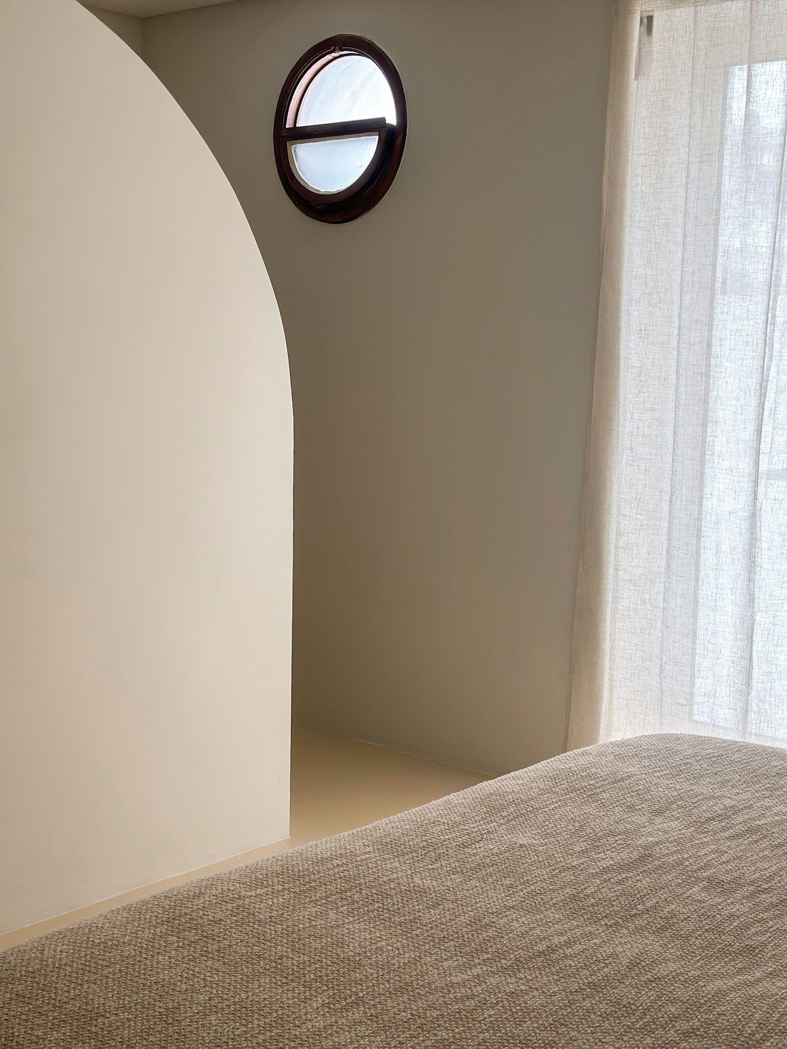 A room with a round window, a curved wall, and a bed with a textured cover.
