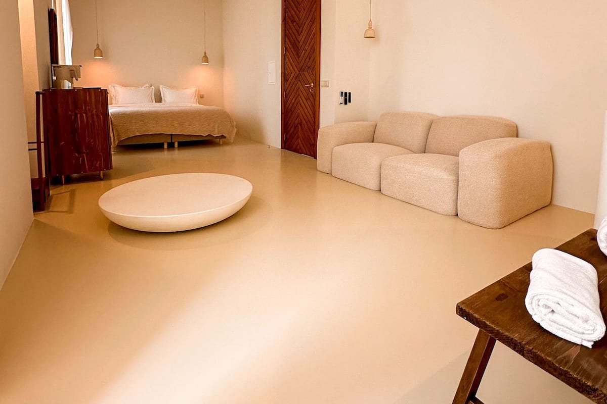 A modern hotel room with a bed, a sofa, a round table, and a wooden cabinet.