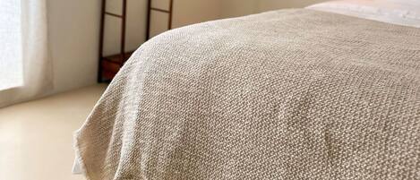 Un dormitorio con una cama, una lámpara colgante y una escalera de madera apoyada en la pared.