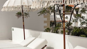 Un área de lounge en la azotea con asientos blancos acolchados y sombrillas blancas.