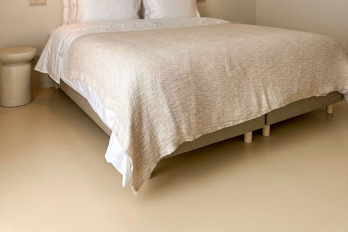 A bedroom with a bed, two pendant lights, an air conditioning unit, and a small bedside table.