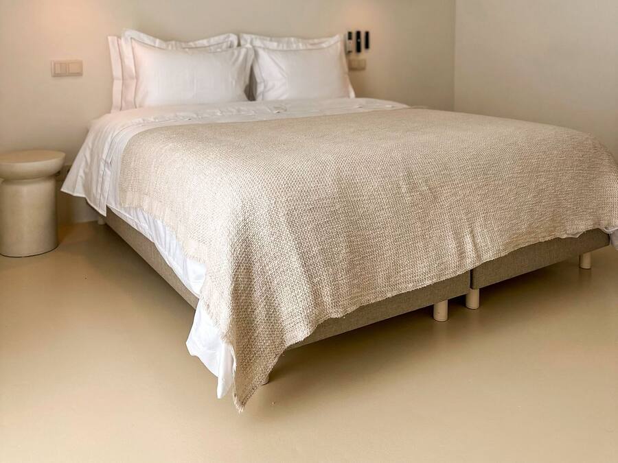 A bedroom with a bed, two pendant lights, an air conditioning unit, and a small bedside table.