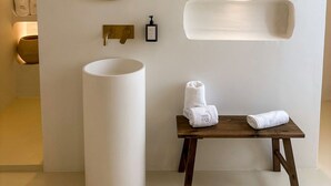 Un baño moderno con un espejo redondo grande, un lavabo blanco y un banco de madera con toallas.