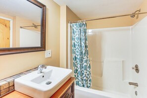 Un baño con un lavabo blanco, un espejo, una ducha con cortina azul estampada y una bañera.