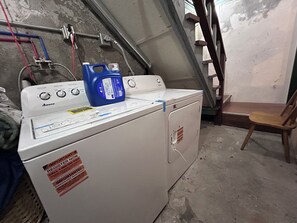 A white washing machine with a blue detergent bottle on top, a warning label, and a chair nearby. - Cozy Loft Studio in a Triplex, near SouthSideWorks (Pittsburgh)