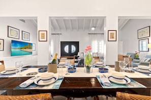 Un coin repas avec une table dressée pour quatre personnes, un téléviseur fixé au mur et des œuvres d’art encadrées qui décorent les murs.