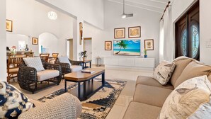 A spacious living room with a large TV, wicker furniture, and a patterned rug.