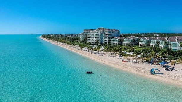 A coastal hotel with a beach view, clear turquoise waters, and a small boat in the distance.