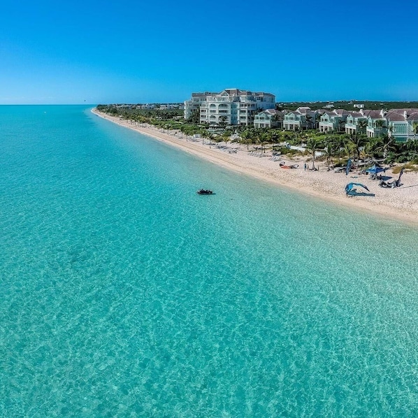 Un hôtel en bord de mer offrant une vue sur la plage, une eau turquoise et limpide, et un petit bateau visible au loin.