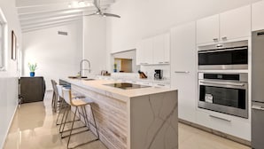A modern kitchen with a central island, bar stools, a ceiling fan, and built-in ovens.
