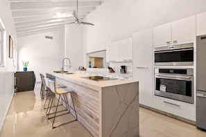 Une cuisine moderne dotée d’un îlot central, de tabourets de bar, d’un ventilateur de plafond et de fours encastrés.