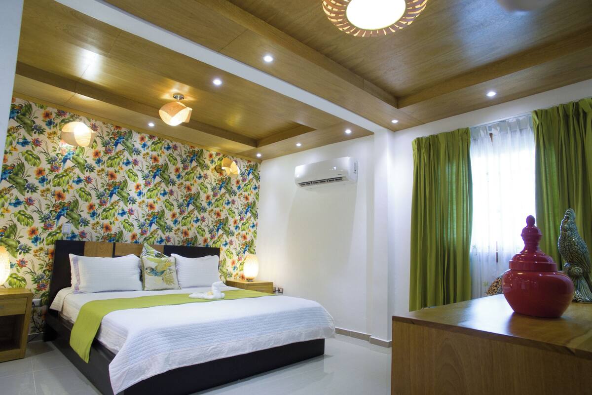 A bedroom with a bed, a nightstand, a wall-mounted air conditioner, and a window with curtains.