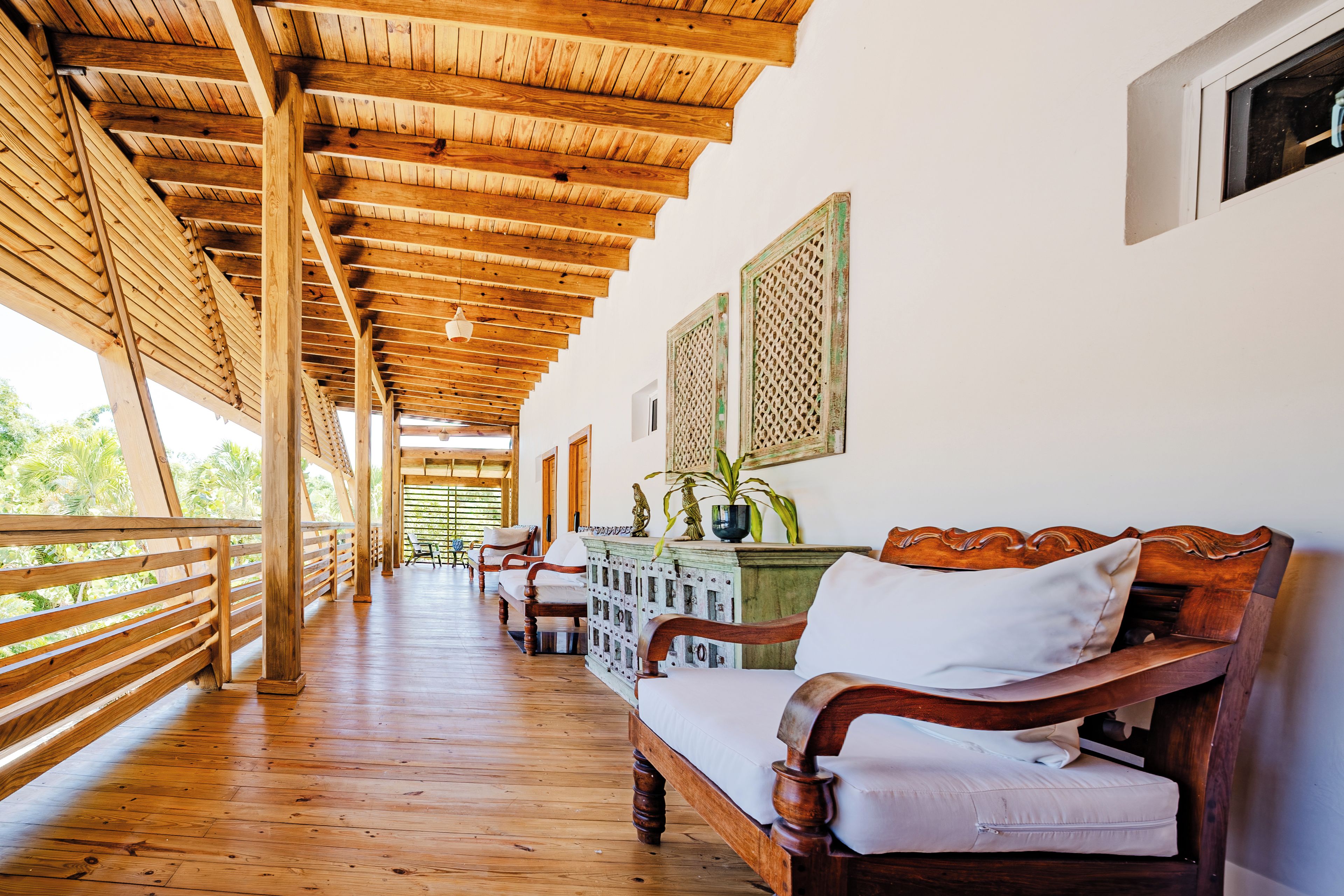 Una terraza de madera con banca y sillas, techo de madera y vista a la vegetación.