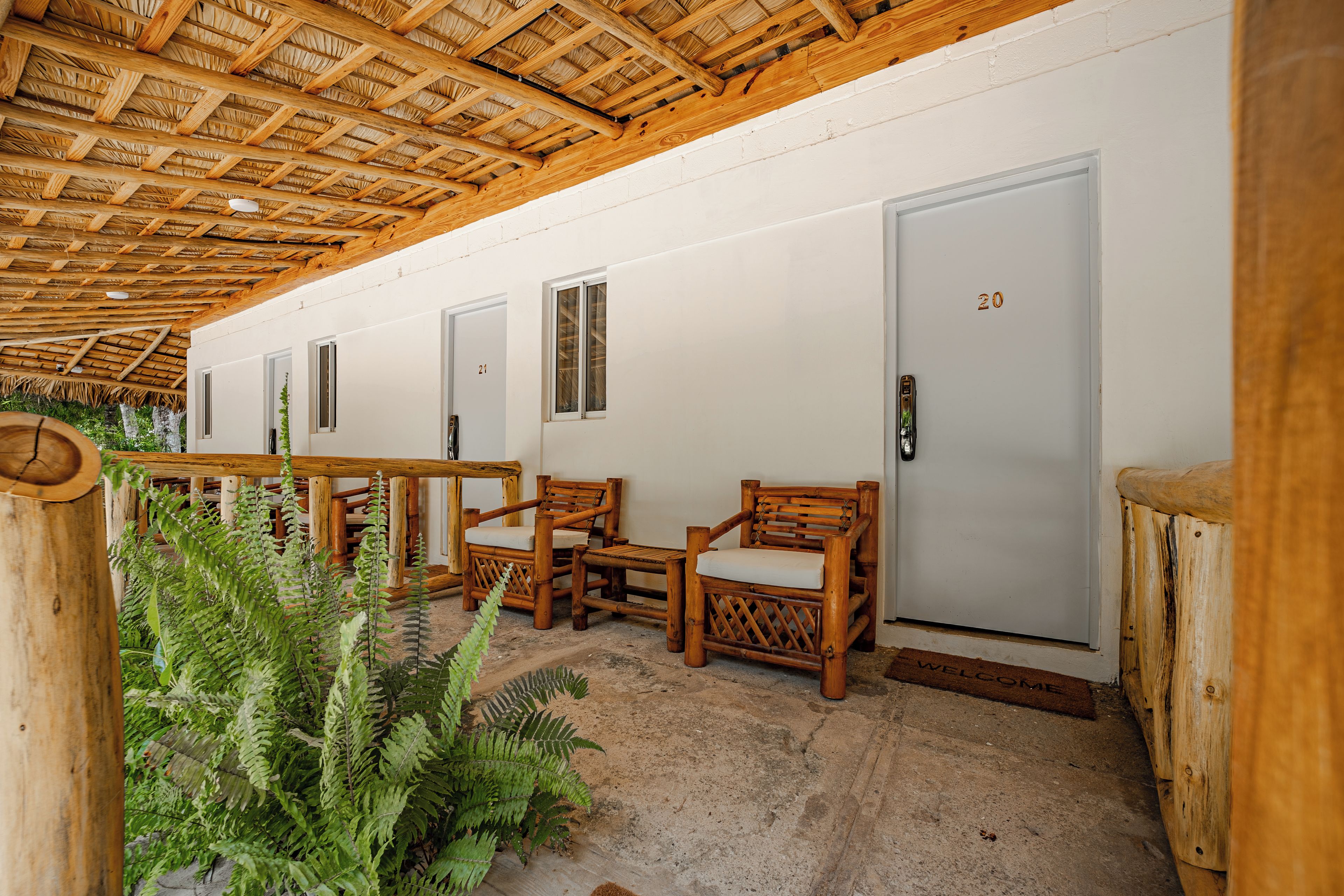 A row of wooden-framed rooms with doors numbered 20 and 21, a wooden bench, and a welcome mat.