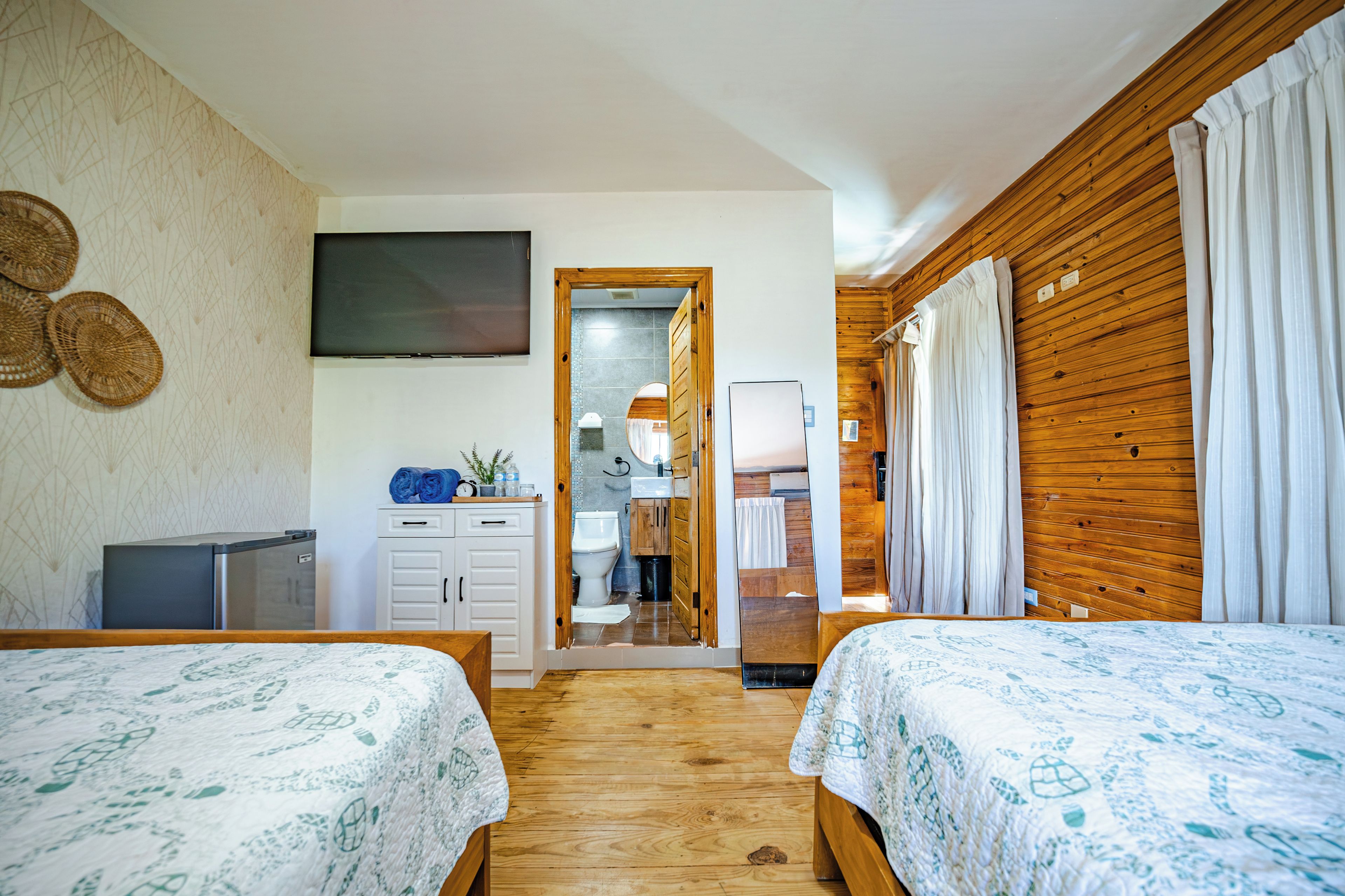 Un dormitorio con dos camas, un televisor, un escritorio pequeño y un baño visible a través de una puerta abierta.