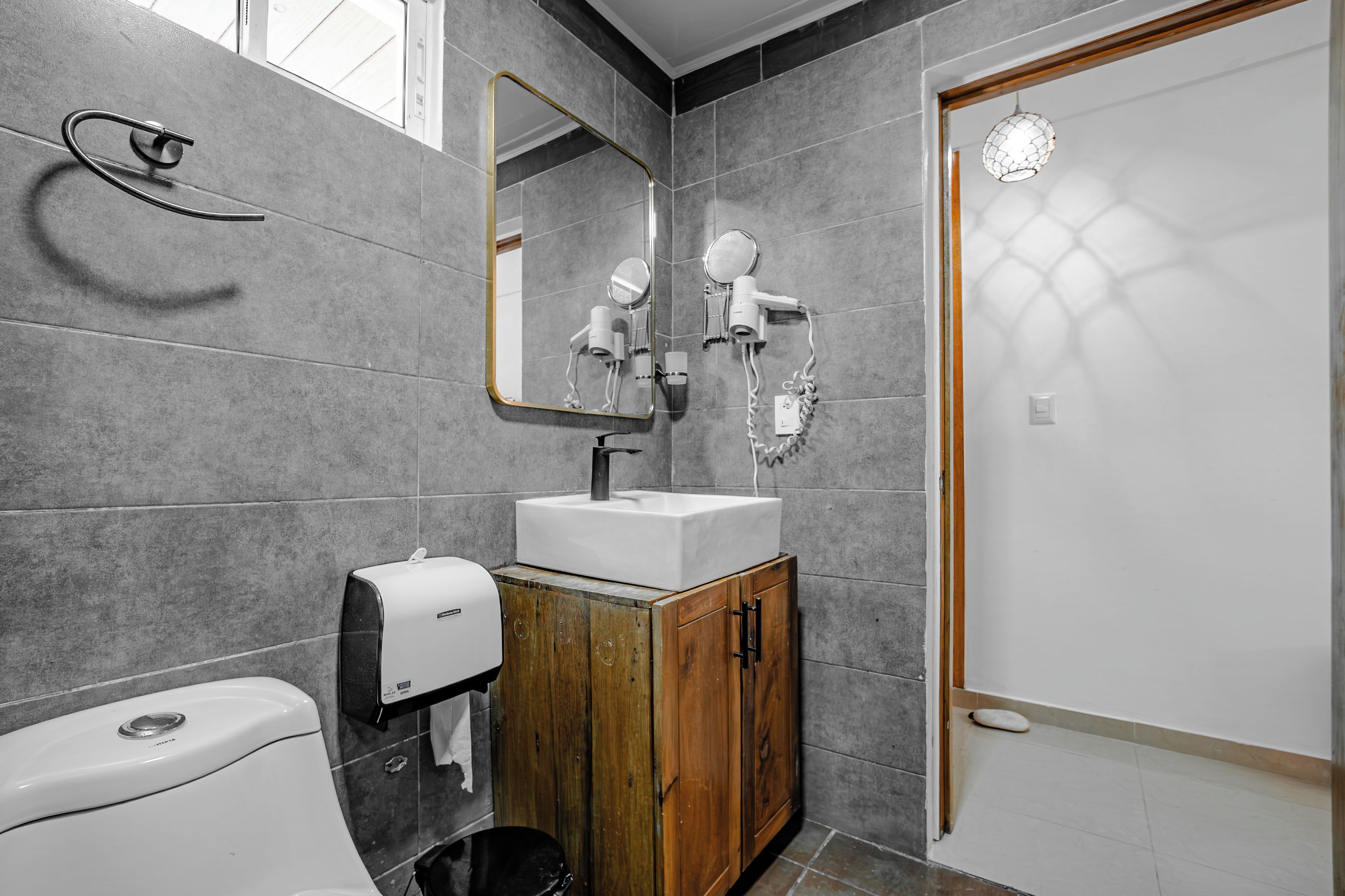 A bathroom with a toilet, sink, mirror, and towel dispenser.