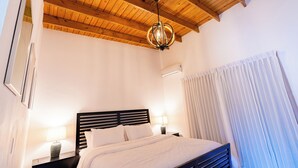 Une chambre avec un plafond en bois, un lit avec une literie blanche, une table de chevet avec une lampe et une fenêtre avec des rideaux.