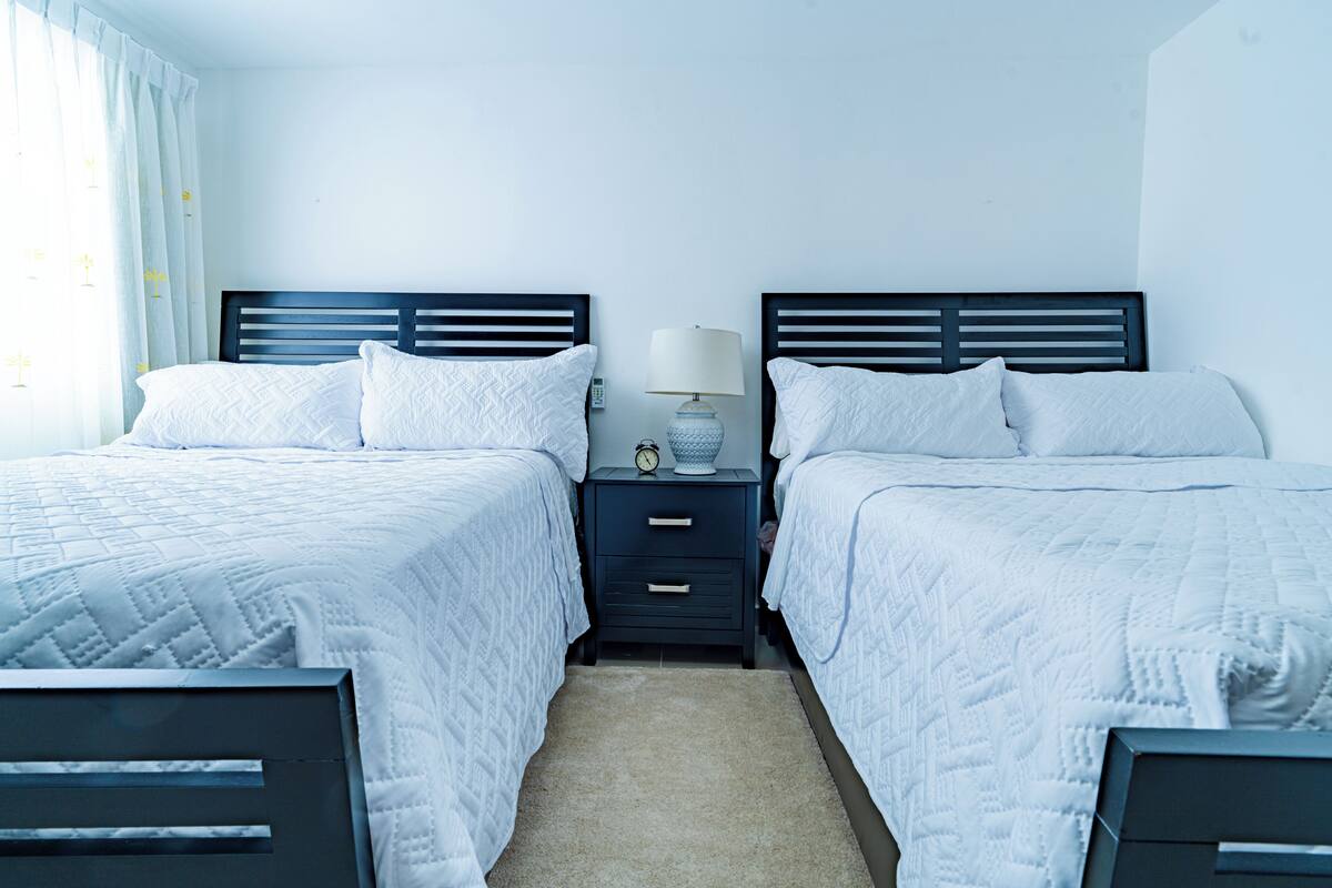 A twin room with two beds, a nightstand with a lamp, and a clock.