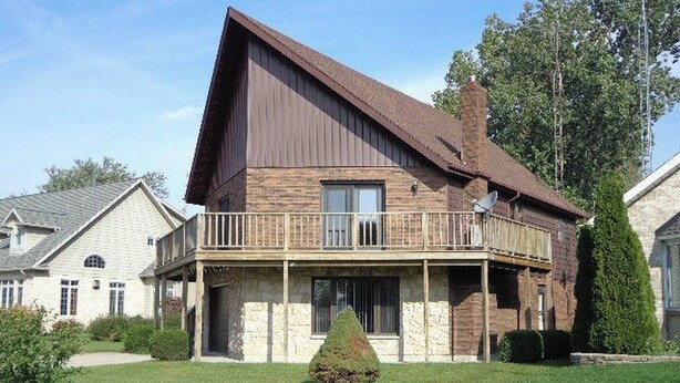 Ein zweistöckiges Haus mit Balkon, SteinFundament und gepflegtem Rasen.
