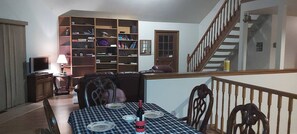 A dining area with a checkered tablecloth, chairs, a wine bottle, and a bookshelf.