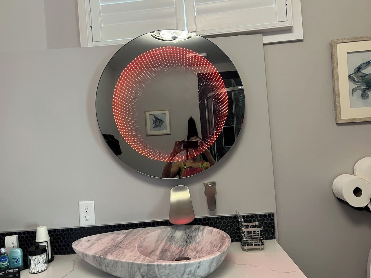Un baño con un espejo redondo, un lavabo de mármol y un dispensador de papel higiénico.