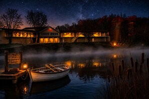 A lakeside lodge with a boat docked at the pier, surrounded by trees and a starry night sky. - Jacuzzi Hot Tub in Main Bedroom! 1,000 Square Feet - Camp Fire - Kayaks & Bikes! (Angola)
