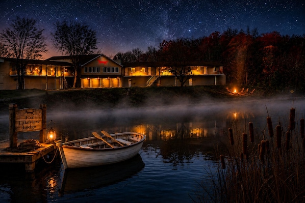 A lakeside lodge with a boat docked at the pier, surrounded by trees and a starry night sky.