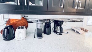 Ett kök med mörka skåp, en bänkskiva i trä, en kaffebryggare, en brödrost och en vattenkokare.