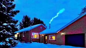 Ett tvåvåningshus med en synlig skorsten, ett garage och en snötäckt uppfart.