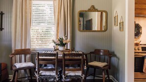 Un comedor con mesa, sillas, un espejo y una ventana con cortinas.